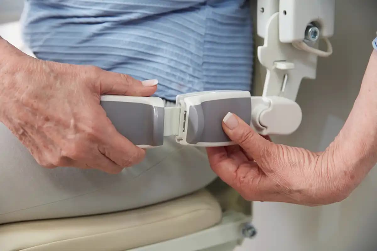 Senior user fastening retractable seatbelt on Savaria Handicare 1100 stairlift with Style Seat and easy-to-use buckle mechanism