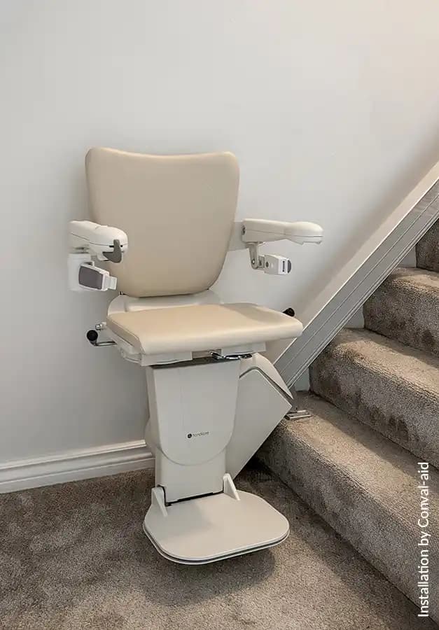 Savaria Handicare 1100 straight stairlift with Style Seat in vanilla beige, slim covered rail with multi-drive system, and folding footrest at bottom landing on carpeted stairs