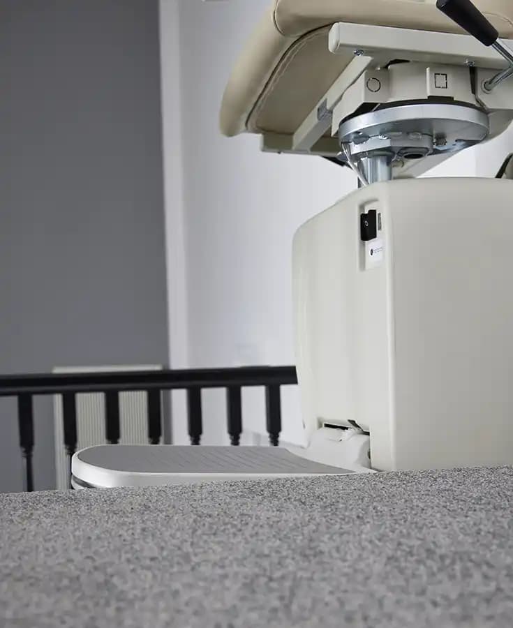Savaria Handicare 4000 curved stairlift carriage mechanism with twin-rail track system, drive motor, and charging contacts on carpeted stairs