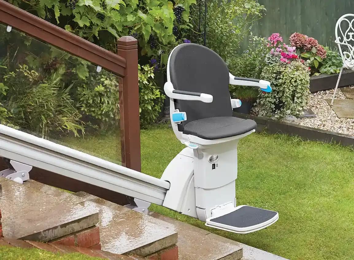 Savaria Handicare 1000 outdoor straight stairlift with Smart Seat in slate upholstery, key switch, power swivel, aluminum rail, and waterproof footrest mat in backyard garden