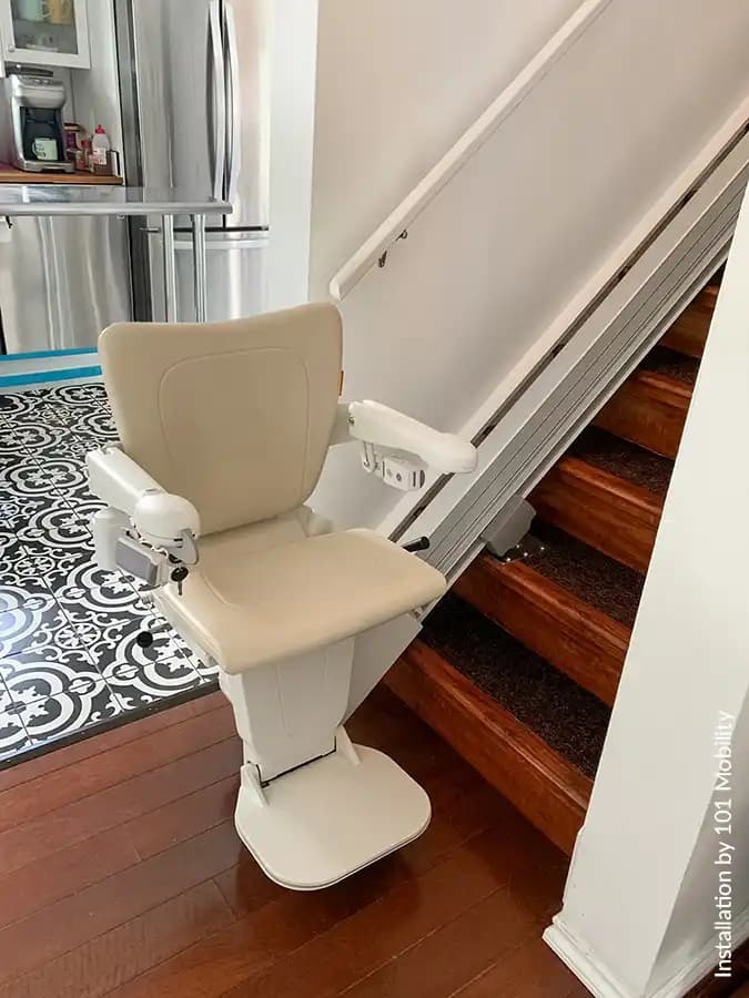 Savaria Handicare 1100 straight stairlift with Style Seat in vanilla beige, slim covered rail with multi-drive system, and folding footrest on residential wood stairs