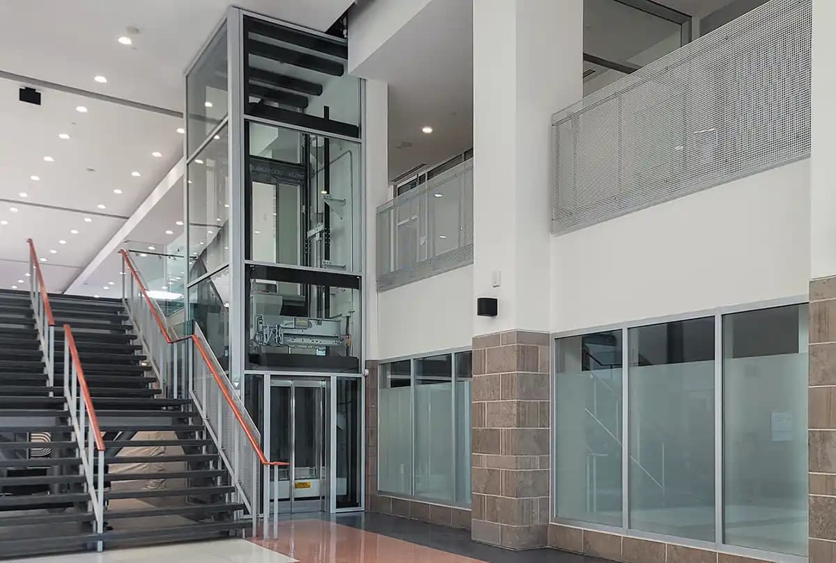 Savaria Orion LU/LA elevator with glass hoistway enclosure, multiple floors visible through transparent shaft in modern commercial building atrium with staircase