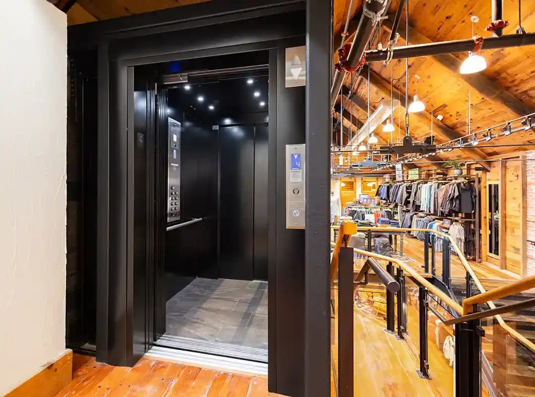 Savaria Orion LU/LA elevator cab with black ceiling, walls, LED recessed lighting, stainless steel handrail, and automatic sliding doors in retail loft interior
