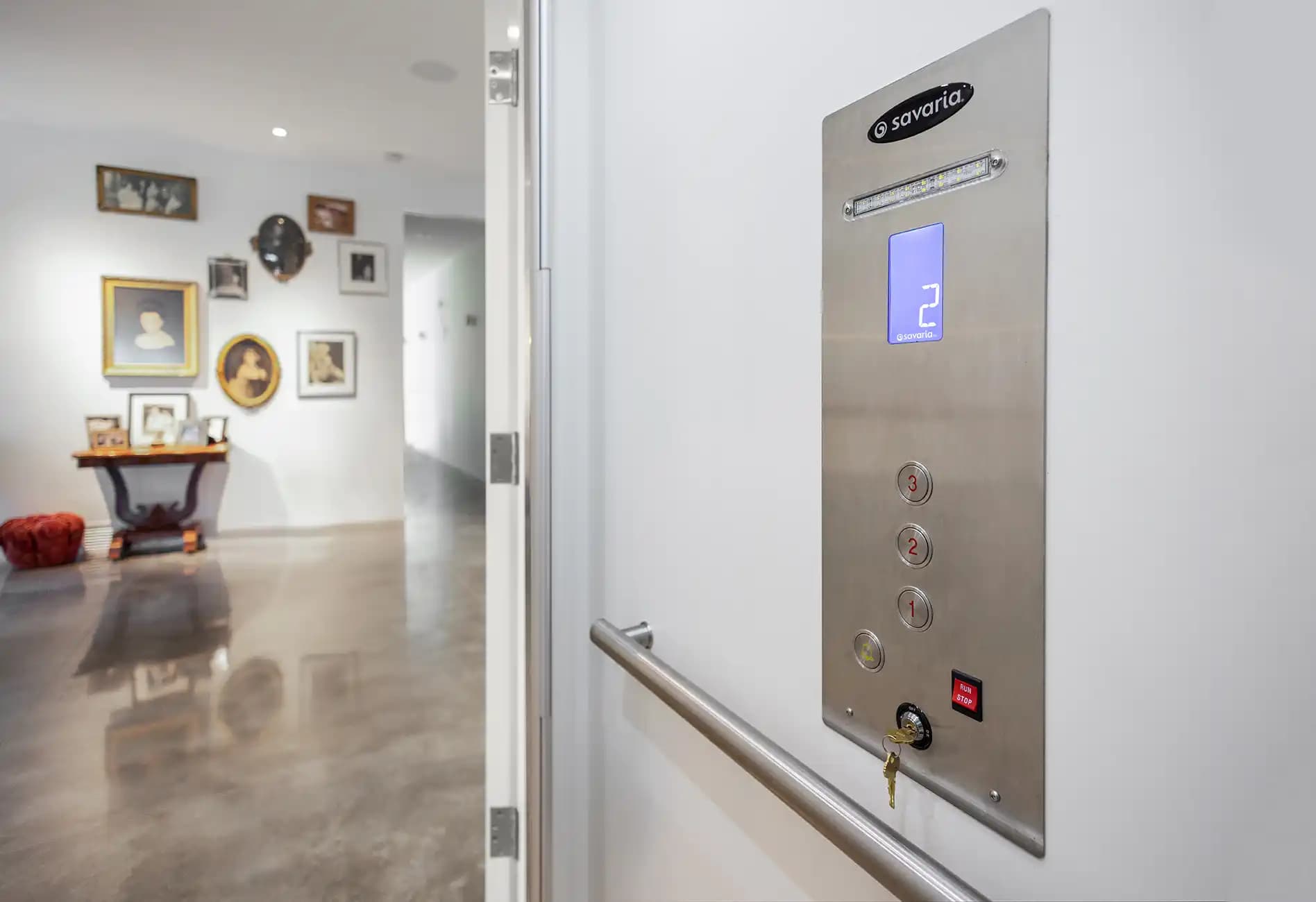 Savaria home elevator car operating panel (COP) with stainless steel finish, digital floor indicator, destination buttons, key switch, and alarm in residential hallway