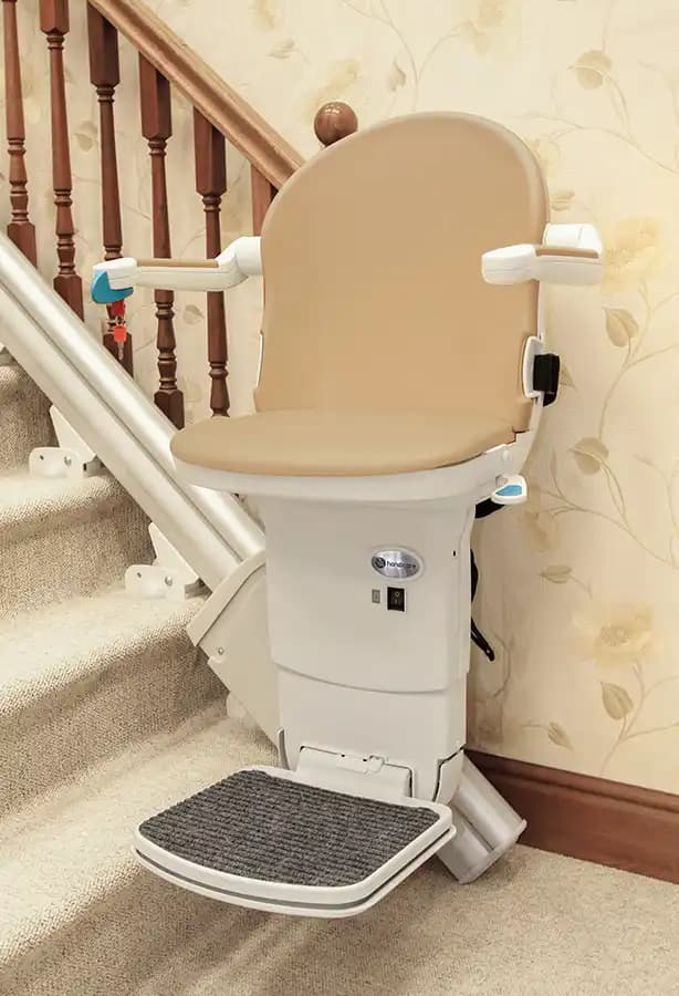 Savaria Handicare 1000 straight stairlift with Smart Seat in sand upholstery, padded armrests, retractable seatbelt, folding footrest, and rack-and-pinion rail on carpeted stairs