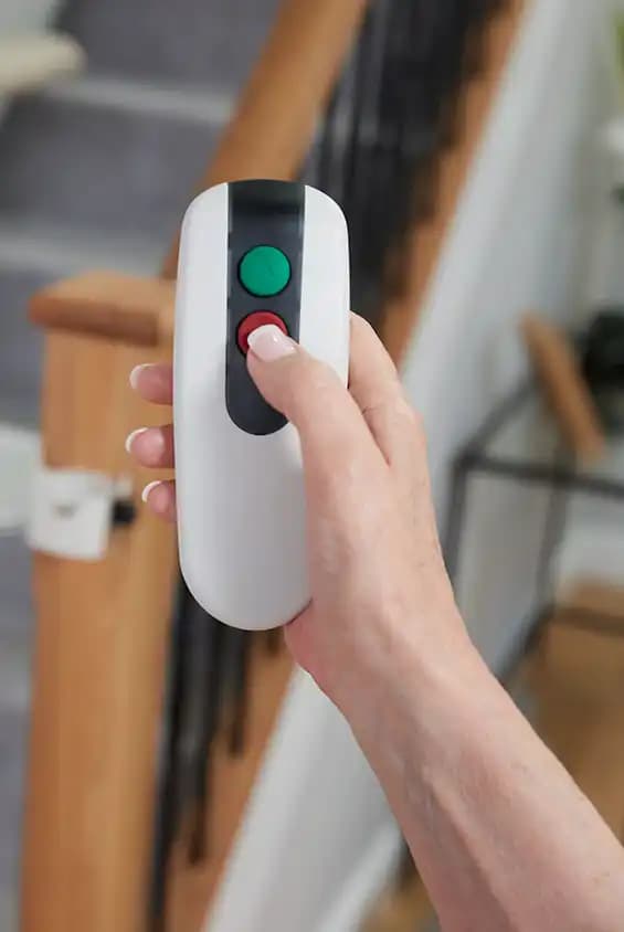 User holding Savaria Handicare stairlift RF remote control with green call button and red stop button for calling chair to different landings