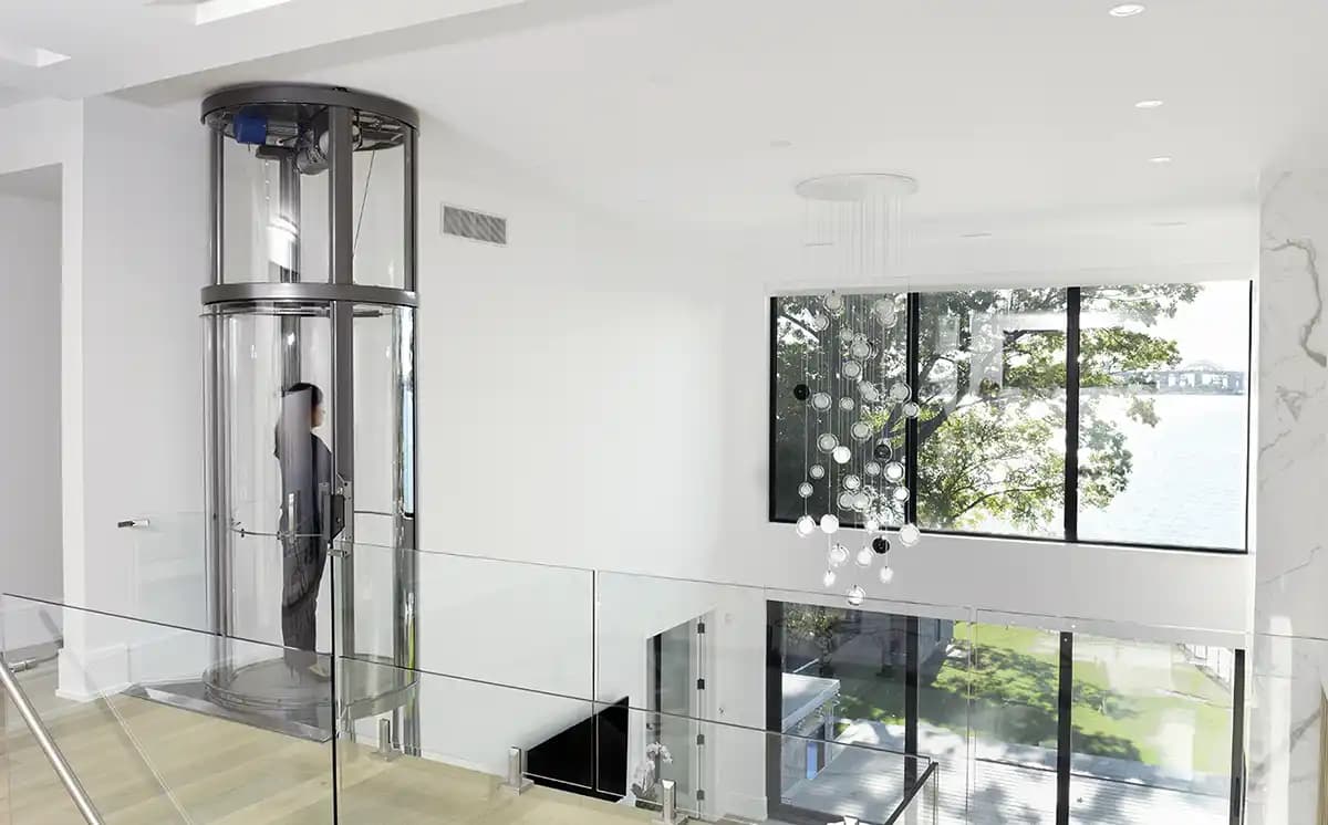 Savaria Vuelift Mini panoramic glass home elevator with integrated hoistway and winding drum drive system in modern residential foyer with glass railings and natural light