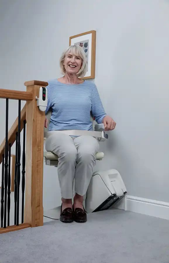 Senior woman riding Savaria Handicare 1100 straight stairlift with Style Seat, retractable seatbelt, and slim covered rail at upper landing